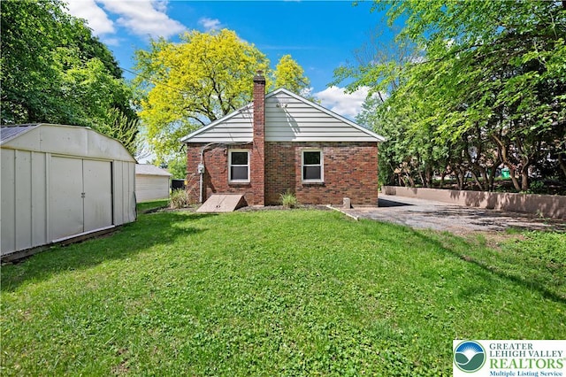 back of house with a shed, a chimney, brick siding, an outbuilding, and a patio