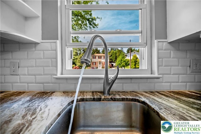 kitchen view of a sink, backsplash, and stone counters