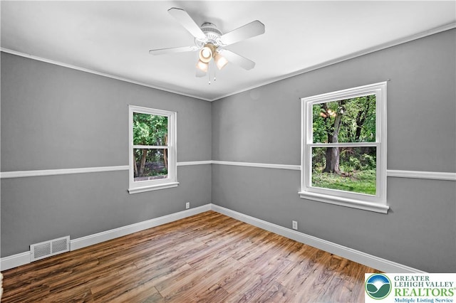 spare room featuring healthy amount of natural light, wood finished floors, baseboards, and crown molding
