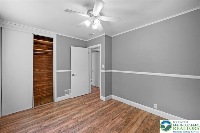 unfurnished bedroom featuring a closet, wood finished floors, baseboards, a ceiling fan, and crown molding