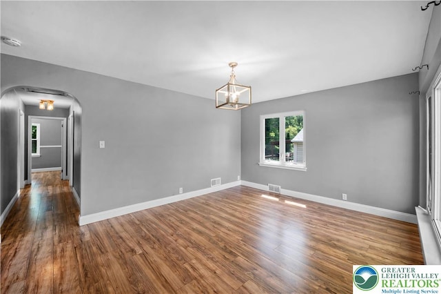 spare room with wood finished floors, a chandelier, a smoke detector, baseboards, and arched walkways