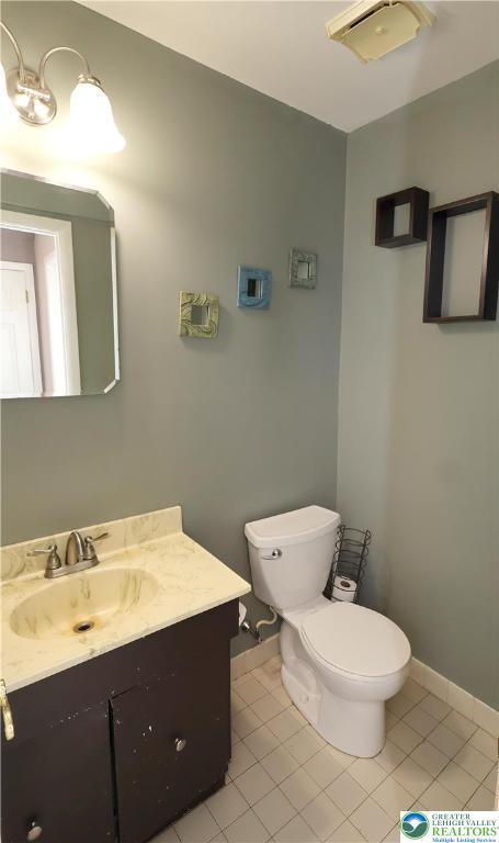 half bath with toilet, vanity, baseboards, and tile patterned flooring