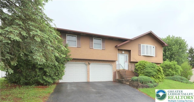 bi-level home with a garage, driveway, brick siding, and a front lawn