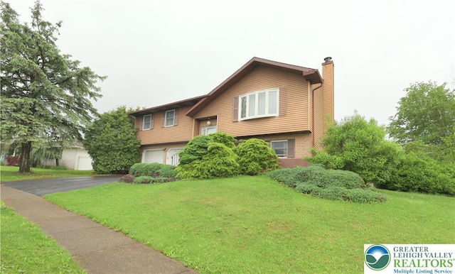 raised ranch with a chimney, a garage, driveway, and a front yard