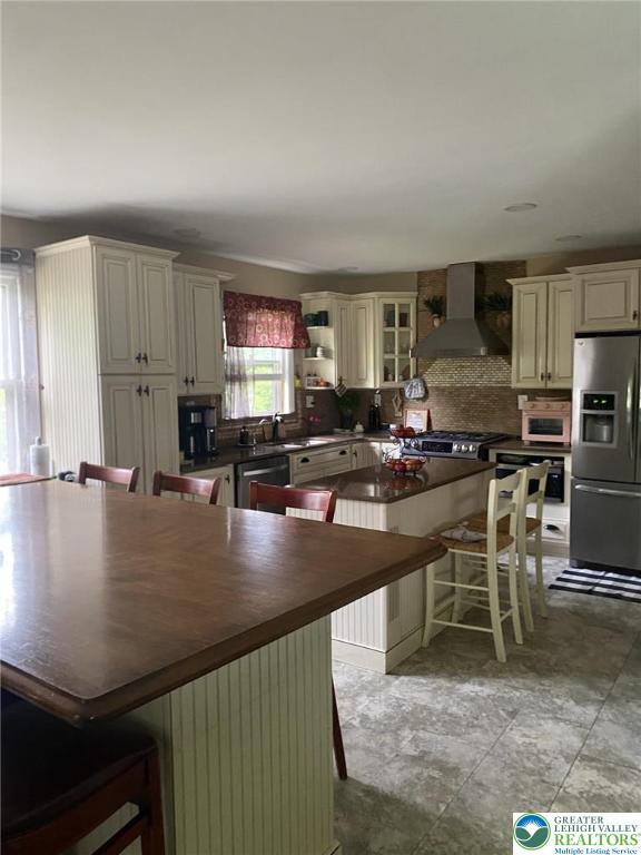 3516 Pine Ave, Saint Lawrence, PA 19606 - kitchen featuring stainless steel appliances, wall chimney exhaust hood, backsplash, a center island, and a kitchen breakfast bar