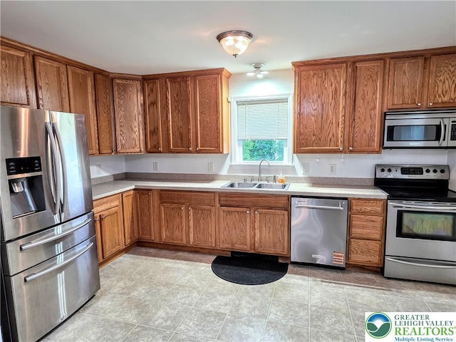 kitchen with appliances with stainless steel finishes, a sink, brown cabinets, and light countertops