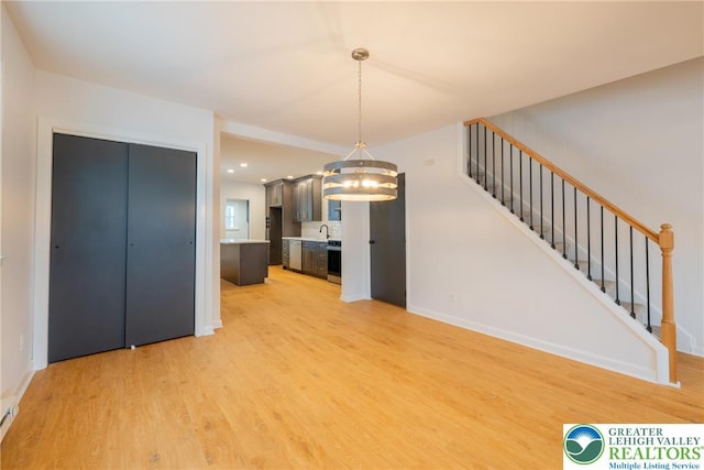 unfurnished living room with light wood-type flooring, a chandelier, stairs, and baseboards