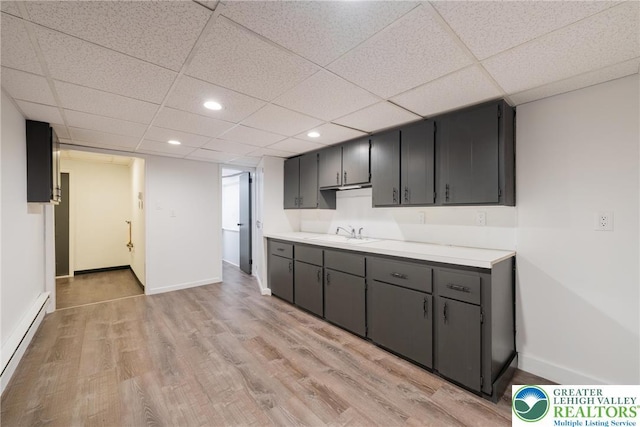 kitchen with a sink, a baseboard radiator, light wood finished floors, baseboards, and light countertops