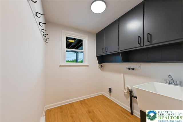clothes washing area with cabinet space, light wood-style floors, and baseboards