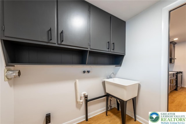 laundry room featuring cabinet space, light wood finished floors, baseboards, and washer hookup