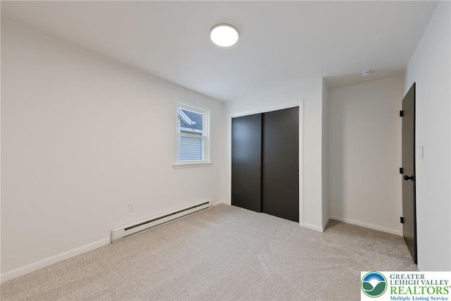 unfurnished bedroom with baseboard heating, light carpet, a closet, and baseboards