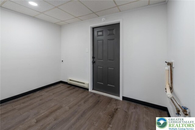 empty room with baseboard heating, a paneled ceiling, dark wood-style floors, and baseboards