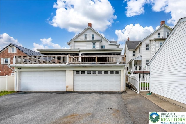 view of front of home featuring asphalt driveway, fence, a chimney, and a balcony