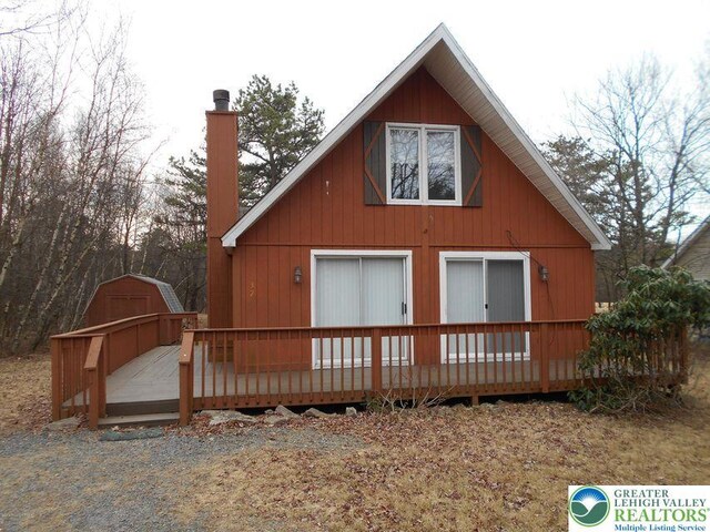 back of property with a storage shed, a deck, a chimney, and an outdoor structure