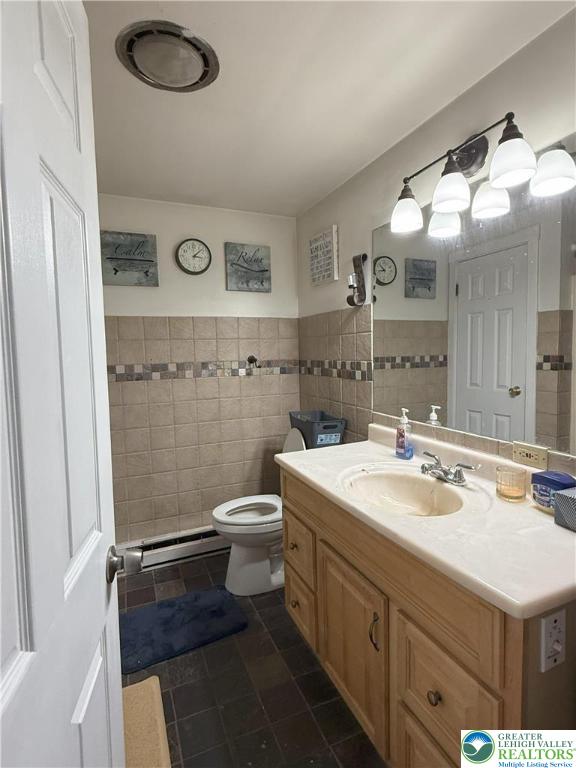 bathroom featuring tile walls, a baseboard heating unit, toilet, vanity, and tile patterned flooring