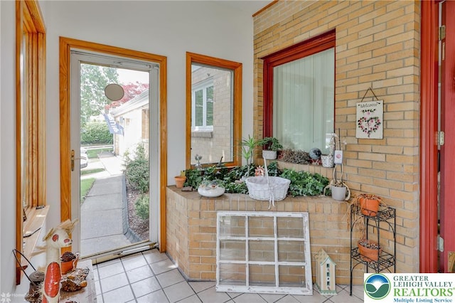 foyer entrance with tile patterned floors and brick wall