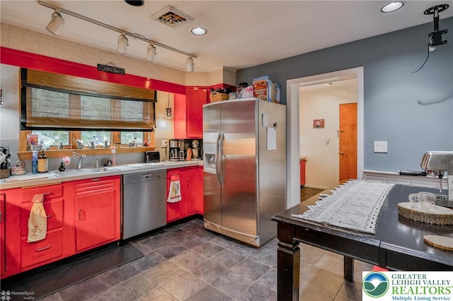 kitchen featuring appliances with stainless steel finishes, a sink, light countertops, red cabinetry, and rail lighting