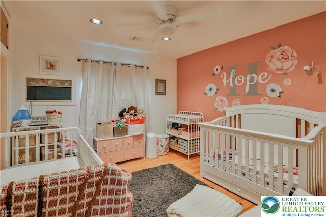 bedroom featuring a nursery area, wood finished floors, recessed lighting, and ceiling fan