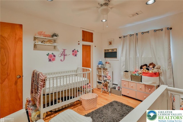 bedroom with a nursery area, wood finished floors, and ceiling fan