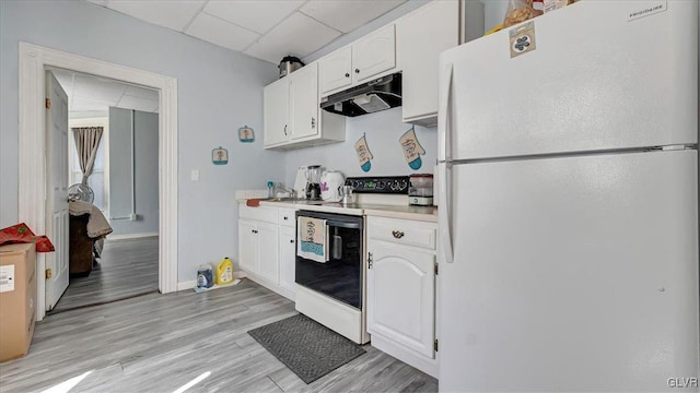 kitchen featuring freestanding refrigerator, under cabinet range hood, range with electric stovetop, a drop ceiling, and white cabinets