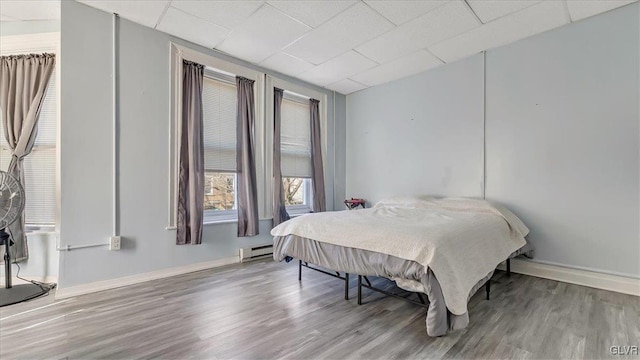 bedroom featuring a baseboard radiator, wood finished floors, a paneled ceiling, and baseboards