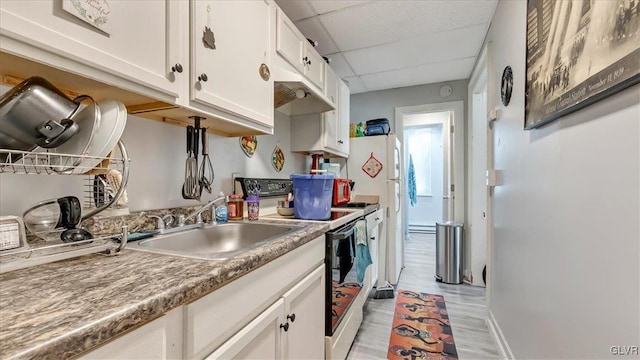 kitchen with electric range, a drop ceiling, white cabinetry, a sink, and light wood-style floors
