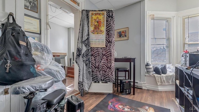 interior space with wood finished floors, multiple windows, a drop ceiling, a baseboard heating unit, and baseboards
