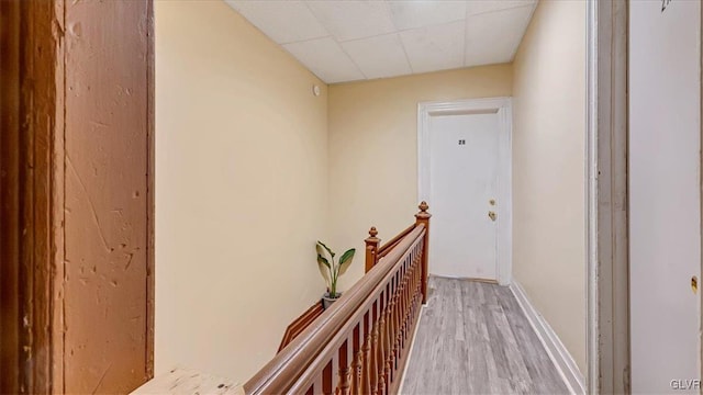 hall with an upstairs landing, light wood-style flooring, a drop ceiling, and baseboards
