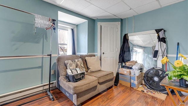 sitting room with a baseboard radiator, wood finished floors, and a drop ceiling