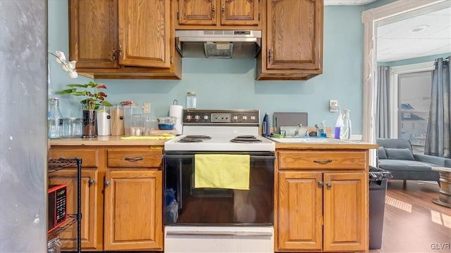 kitchen with electric range, under cabinet range hood, light countertops, and brown cabinetry