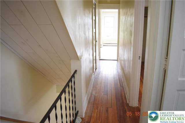 corridor with an upstairs landing, wood-type flooring, and a baseboard heating unit