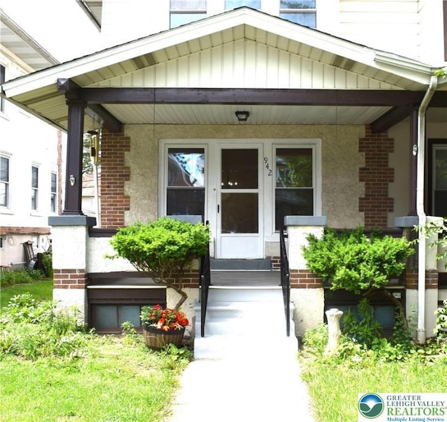 view of exterior entry featuring covered porch and brick siding