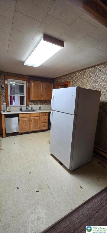 kitchen with freestanding refrigerator, dishwasher, brown cabinets, wallpapered walls, and a sink