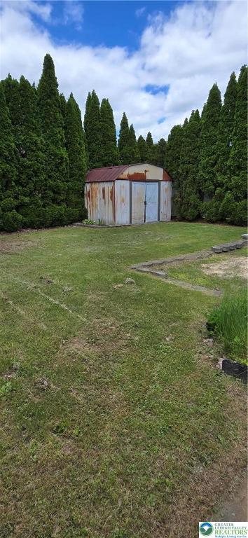 view of grassy yard featuring an outbuilding and a forest view
