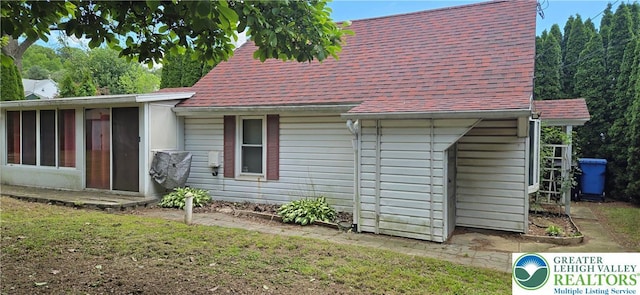 view of side of home featuring a sunroom, a yard, and roof with shingles