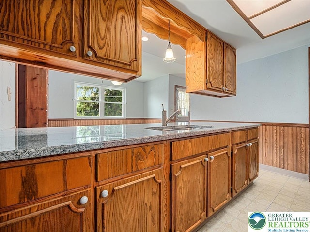 1218 Avocet Dr, Upper Macungie Twp, PA 18031 - kitchen with brown cabinetry, a sink, a wainscoted wall, wood walls, and stone counters