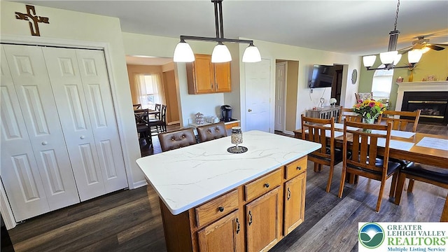4125 Redbud Dr W, Whitehall Twp, PA 18052 - kitchen with dark wood finished floors, a center island, hanging light fixtures, a glass covered fireplace, and light stone counters