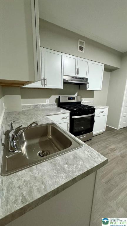 836 Elliger St, Allentown City, PA 18102 - kitchen featuring stainless steel range with gas cooktop, under cabinet range hood, a sink, white cabinets, and light countertops