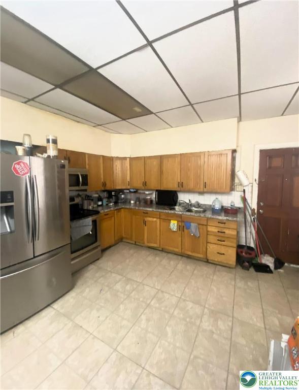 726 N 8th St, Allentown City, PA 18102 - kitchen with stainless steel appliances, brown cabinets, a paneled ceiling, dark countertops, and light tile patterned flooring