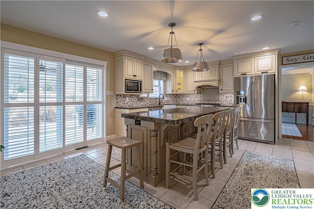 4408 Irish Creek Rd, Pa, PA 19506 - kitchen featuring appliances with stainless steel finishes, cream cabinetry, light tile patterned flooring, decorative backsplash, and a breakfast bar area