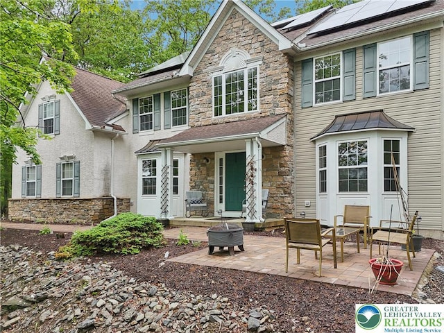 136 Outlook Ct, Middle Smithfield Twp, PA 18302 - back of property with stone siding, solar panels, a patio, a fire pit, and a standing seam roof