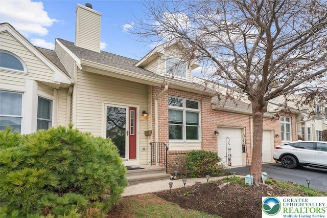 275 Ridings Cir, Macungie Borough, PA 18062 - view of front facade with a chimney, brick siding, driveway, an attached garage, and a shingled roof
