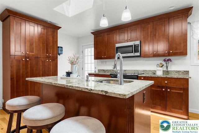 3079 Eldridge Ave, Palmer Twp, PA 18045 - kitchen with stainless steel microwave, light wood-style floors, a skylight, pendant lighting, and a kitchen island with sink
