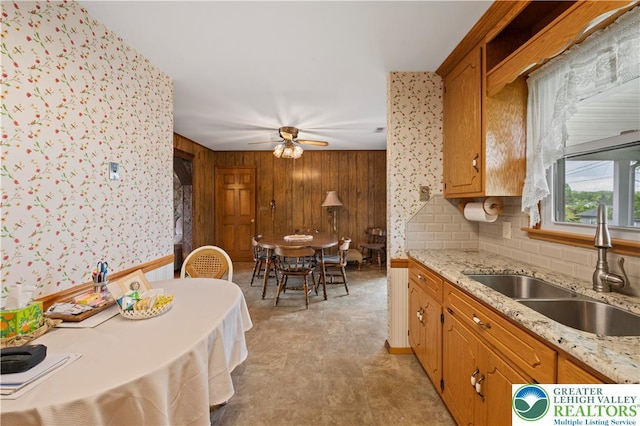 155 7th St, Tatamy Borough, PA 18085 - kitchen with a sink, ceiling fan, wooden walls, brown cabinetry, and light stone counters