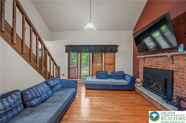 1117 Belaire Dr, Stroud Twp, PA 18301 - living area with vaulted ceiling, a brick fireplace, hardwood / wood-style flooring, stairway, and a textured ceiling