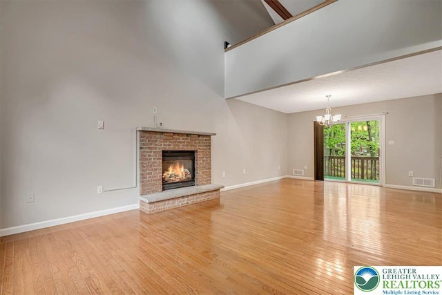 2330 Burntwood Dr, East Stroudsburg, PA 18301 - unfurnished living room with a chandelier, wood finished floors, a brick fireplace, and a towering ceiling