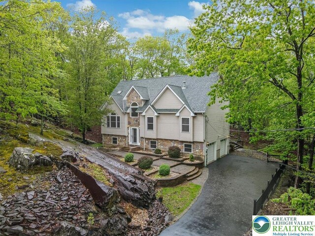 2330 Burntwood Dr, East Stroudsburg, PA 18301 - view of front facade featuring stone siding, an attached garage, driveway, and roof with shingles