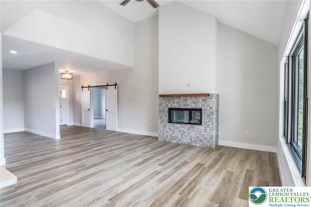 448 Long Lane Rd, Lehigh Twp, PA 18088 - unfurnished living room with a barn door, wood finished floors, high vaulted ceiling, a stone fireplace, and a ceiling fan