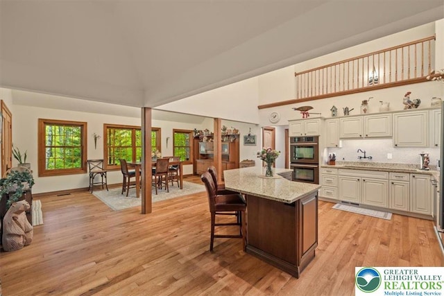 127 Timber Lake Dr, Barrett Twp, PA 18325 - kitchen with stainless steel double oven, a towering ceiling, light wood-style flooring, light stone countertops, and a kitchen island