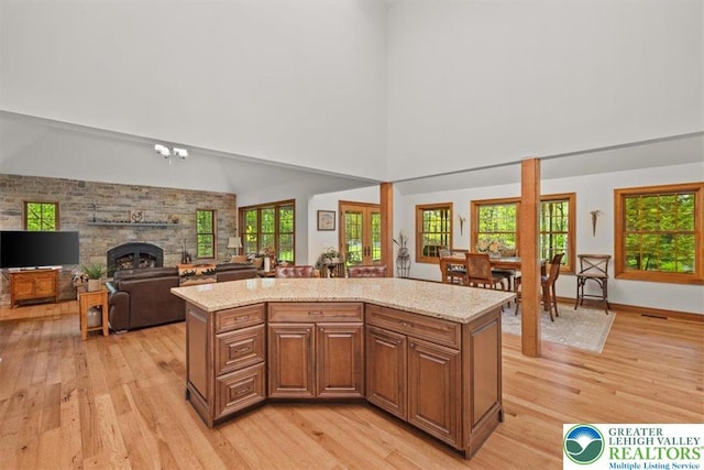 127 Timber Lake Dr, Barrett Twp, PA 18325 - kitchen featuring light wood-style flooring, a kitchen island, light stone counters, a stone fireplace, and a towering ceiling